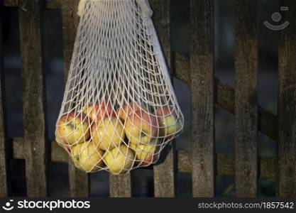 bag from macrame with apples hanging on the fence against the backdrop of the vegetable garden. aesthetics of rural life