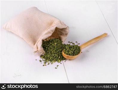 bag with dried green spices and a wooden spoon on a white kitchen table