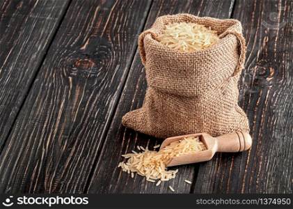 Bag with long rice and spoon stands on wooden background. Bag with rice and spoon stands