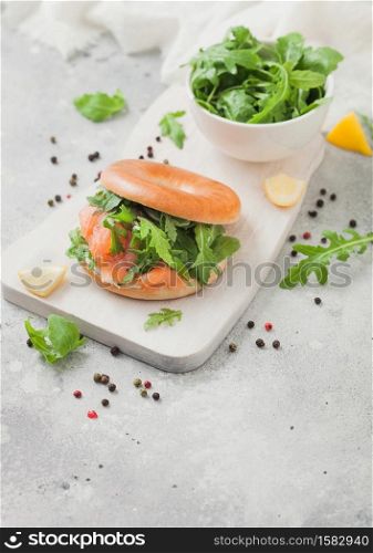 Bagel and salmon sandwich with cream cheese and wild rocket in white bowl and lemon with pepper.