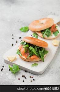 Bagel and salmon sandwiches with cream cheese and wild rocket and lemon with pepper on light kitchen background.