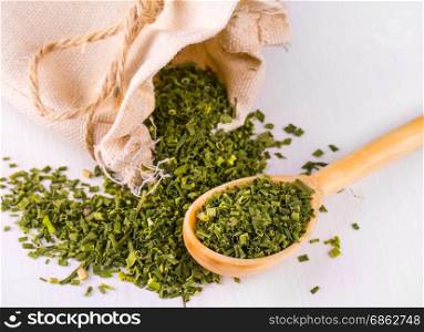 Baggy sack with dried green spices and a wooden spoon on a white kitchen table