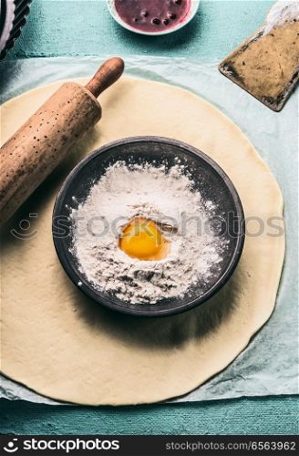 Bake concept. Dough, rolling pin and bowl with flour and egg, top view