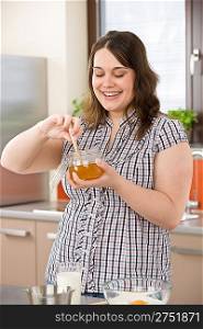 Bake - happy woman with ingredients in kitchen prepare cake holding honey jar