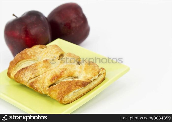 Baked apple strudel on light green plate with 2 red apples behind. Horizontal image with white copy space.
