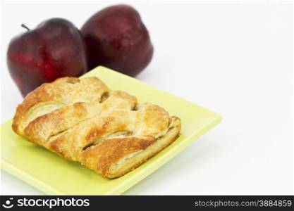 Baked apple strudel on light green plate with 2 red apples behind. Horizontal image with white copy space.