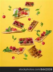 Baked Belgian waffles, raspberries and mint leaves levitate on a yellow background