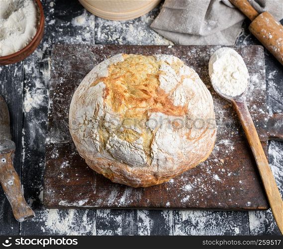 baked bread, white wheat flour, wooden rolling pin and old cutting board on a black table, top view