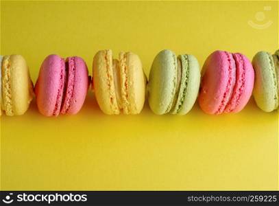 baked cakes of almond flour with cream on a yellow background, dessert macarons lies in a row in the middle