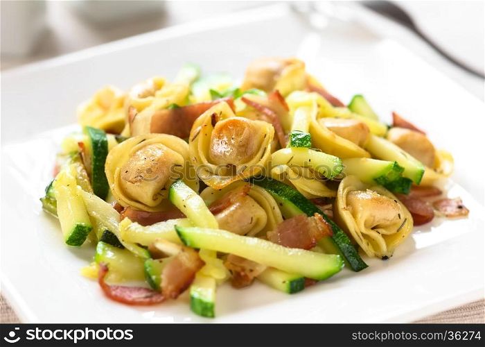 Baked cheese tortellini or belly button pasta with zucchini, bacon and thyme, photographed with natural light (Selective Focus, Focus on the tortellini on the top)