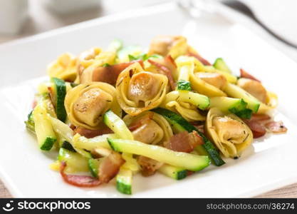 Baked cheese tortellini or belly button pasta with zucchini, bacon and thyme, photographed with natural light (Selective Focus, Focus on the tortellini on the top)