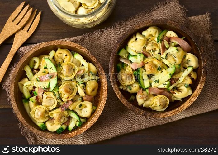 Baked cheese tortellini or belly button pasta with zucchini, bacon and thyme in wooden bowls, photographed overhead on dark wood with natural light (Selective Focus, Focus on the top of the dishes)