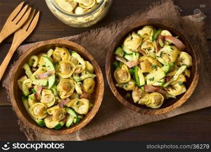 Baked cheese tortellini or belly button pasta with zucchini, bacon and thyme in wooden bowls, photographed overhead on dark wood with natural light (Selective Focus, Focus on the top of the dishes)
