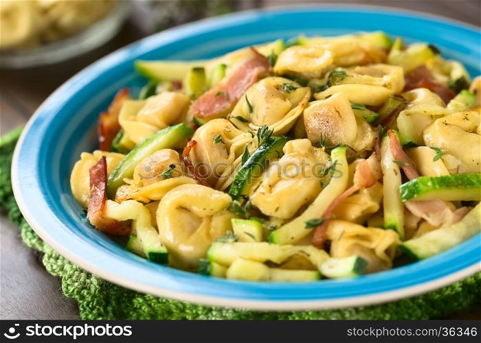Baked cheese tortellini or belly button pasta with zucchini, bacon and thyme, photographed with natural light (Selective Focus, Focus in the middle of the dish)