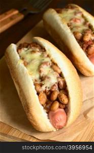 Baked chili hot dogs on wooden board, photographed with natural light (Selective Focus, Focus on the first beans and the front of the cheese)