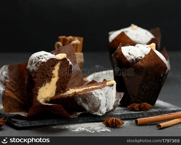 baked chocolate muffin with cream filling sprinkled with powdered sugar on a black table, delicious dessert