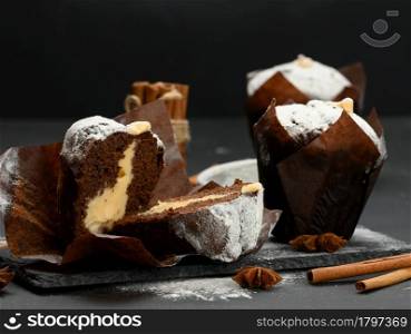 baked chocolate muffin with cream filling sprinkled with powdered sugar on a black table, delicious dessert