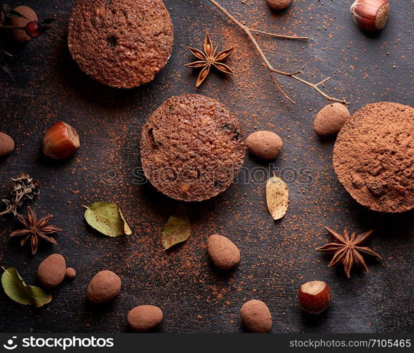 baked chocolate round muffins on a black background, pastries sprinkled with cocoa, top view