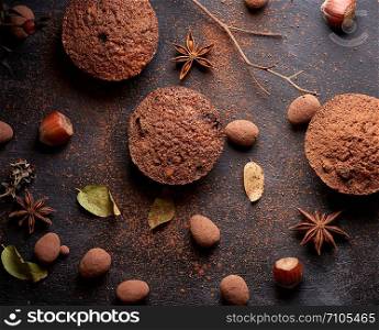 baked chocolate round muffins on a black background, pastries sprinkled with cocoa, top view
