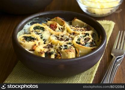 Baked crepe rolls casserole filled with spinach, tomato and mincemeat with cream sauce and grated cheese on top, served in rustic bowl, photographed with natural light (Selective Focus, Focus on the front of the middle roll)
