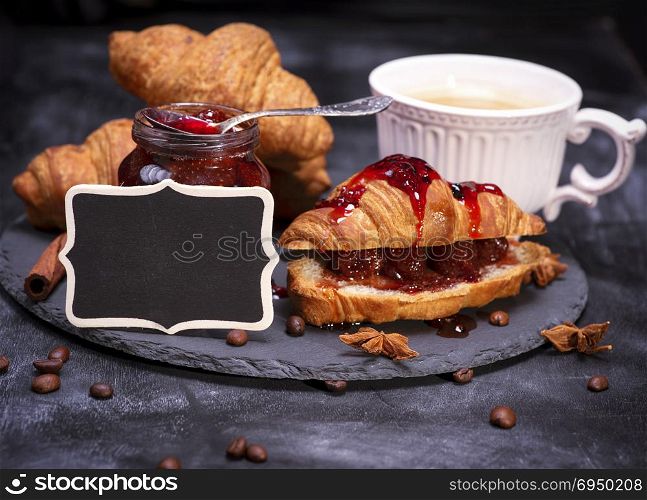 baked crispy croissants with raspberry jam and black empty wooden plaque, black background