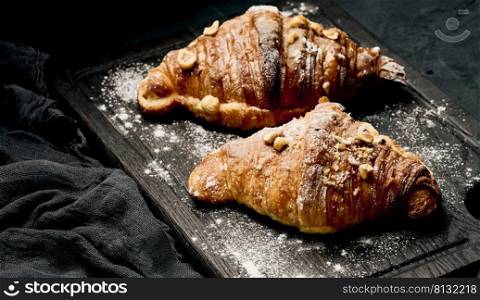 baked croissant on a wooden board and sprinkled with powdered sugar, black table. Appetizing pastries for breakfast