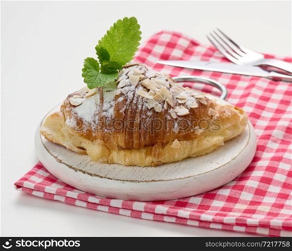 Baked croissant sprinkled with sugar on wooden board, red napkin