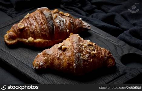 Baked croissants on a black wooden board sprinkled with powdered sugar, close up
