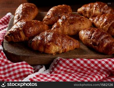 baked croissants on a wooden brown board, delicious and appetizing pastries