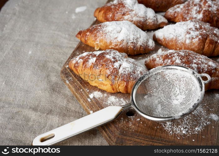 baked croissants sprinkled with powdered sugar lie on a brown wooden board, close up