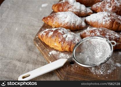 baked croissants sprinkled with powdered sugar lie on a brown wooden board, close up