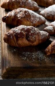 baked croissants sprinkled with powdered sugar lie on a brown wooden board, close up