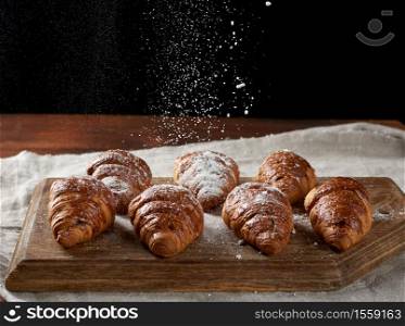 baked croissants sprinkled with powdered sugar on a wooden board, sugar flies from above
