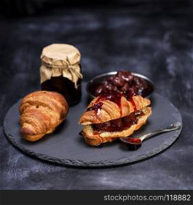 baked croissants with strawberry jam on a black graphite plate. baked croissants with strawberry jam