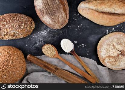 baked different loaves of bread on a black background, empty space in the middle, top view