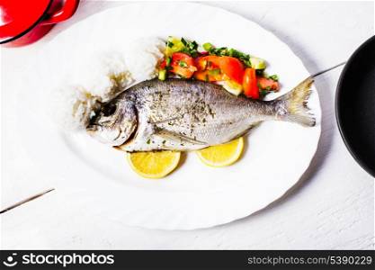 Baked dorado fish with rice and salad on the white plate