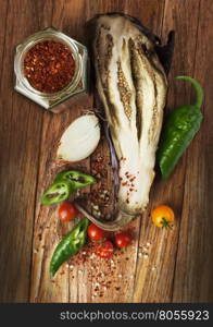 Baked eggplant with tomatoes cherry, onions and chili pepper on wooden table