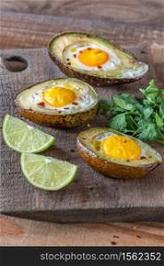 Baked eggs in avocado on the wooden board: top view