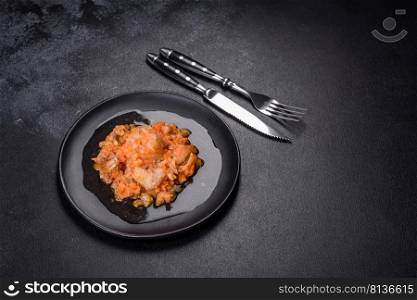 Baked hake white fish with tomato n the black background. A delicious dish of hake fish in chunks in tomato sauce with spices and herbs