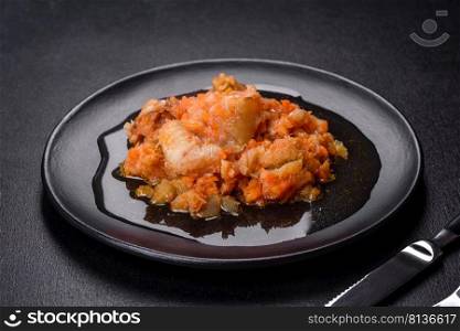 Baked hake white fish with tomato n the black background. A delicious dish of hake fish in chunks in tomato sauce with spices and herbs