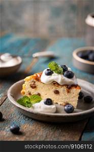 Baked homemade cottage cheese casserole or pudding with raisins serving with blueberry and sour cream on blue background. Close-up.. Cottage cheese casserole