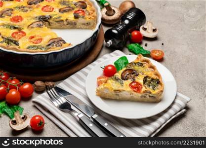 Baked homemade quiche pie with tomato, chcken and mushrooms in ceramic baking form and slice on concrete background. Baked homemade quiche pie in ceramic baking form and slice