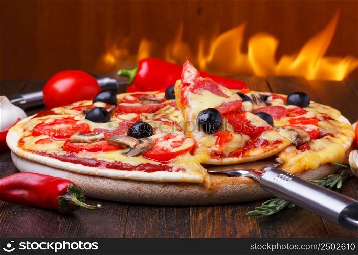 Baked hot pizza with one slice on lifter with fire on background