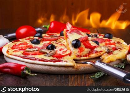 Baked hot pizza with one slice on lifter with fire on background