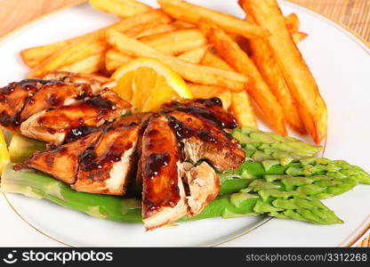 Baked, marinaded chicken breasts with orange and soy sauce, served with french fries on a bed of asparagus