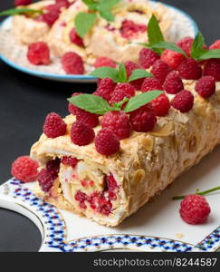 Baked meringue roll with cream and fresh red raspberry on a black wooden board, delicious dessert 
