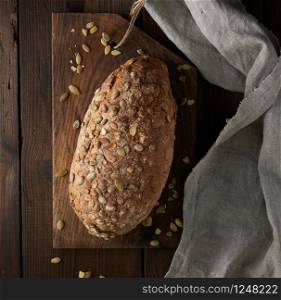 baked oval bread made from rye flour with pumpkin seeds on a gray linen napkin, top view