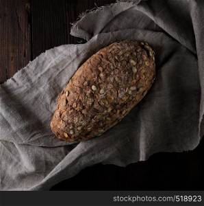 baked oval bread made from rye flour with pumpkin seeds on a gray linen napkin, top view