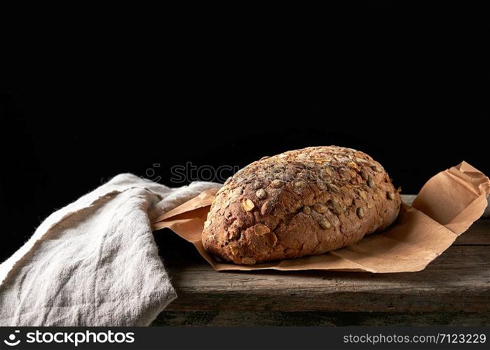 baked oval bread made from rye flour with pumpkin seeds on a gray linen napkin, black background