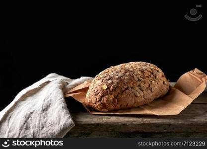 baked oval bread made from rye flour with pumpkin seeds on a gray linen napkin, black background